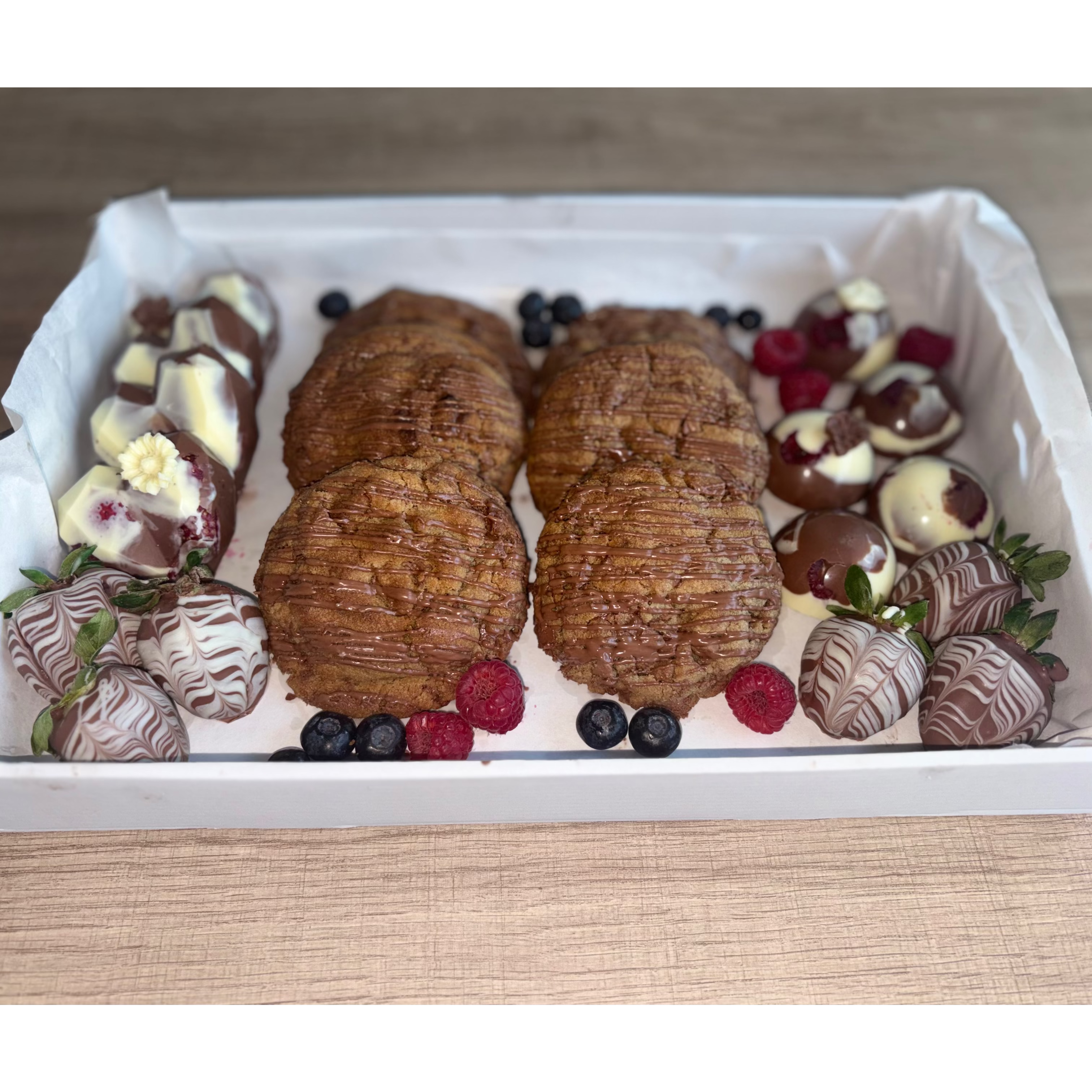 Mixed treats gift box with chocolate-covered strawberries, chocolate chip cookies and fresh berries.